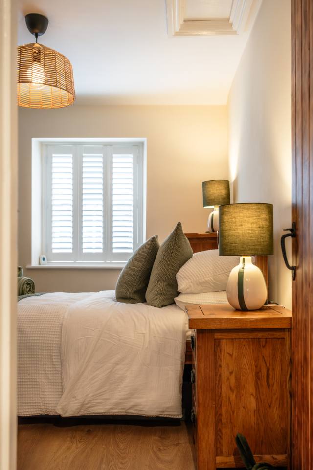 Bright double bedroom in the one-bedroom Glastonbury holiday cottage, with green cushions and bedside lamps