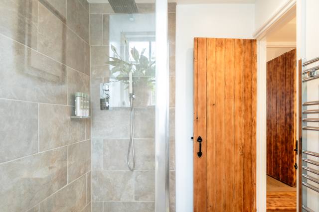 Walk-in rainfall shower at the Glastonbury cottage, with stone-effect tiles and the original pine latch door