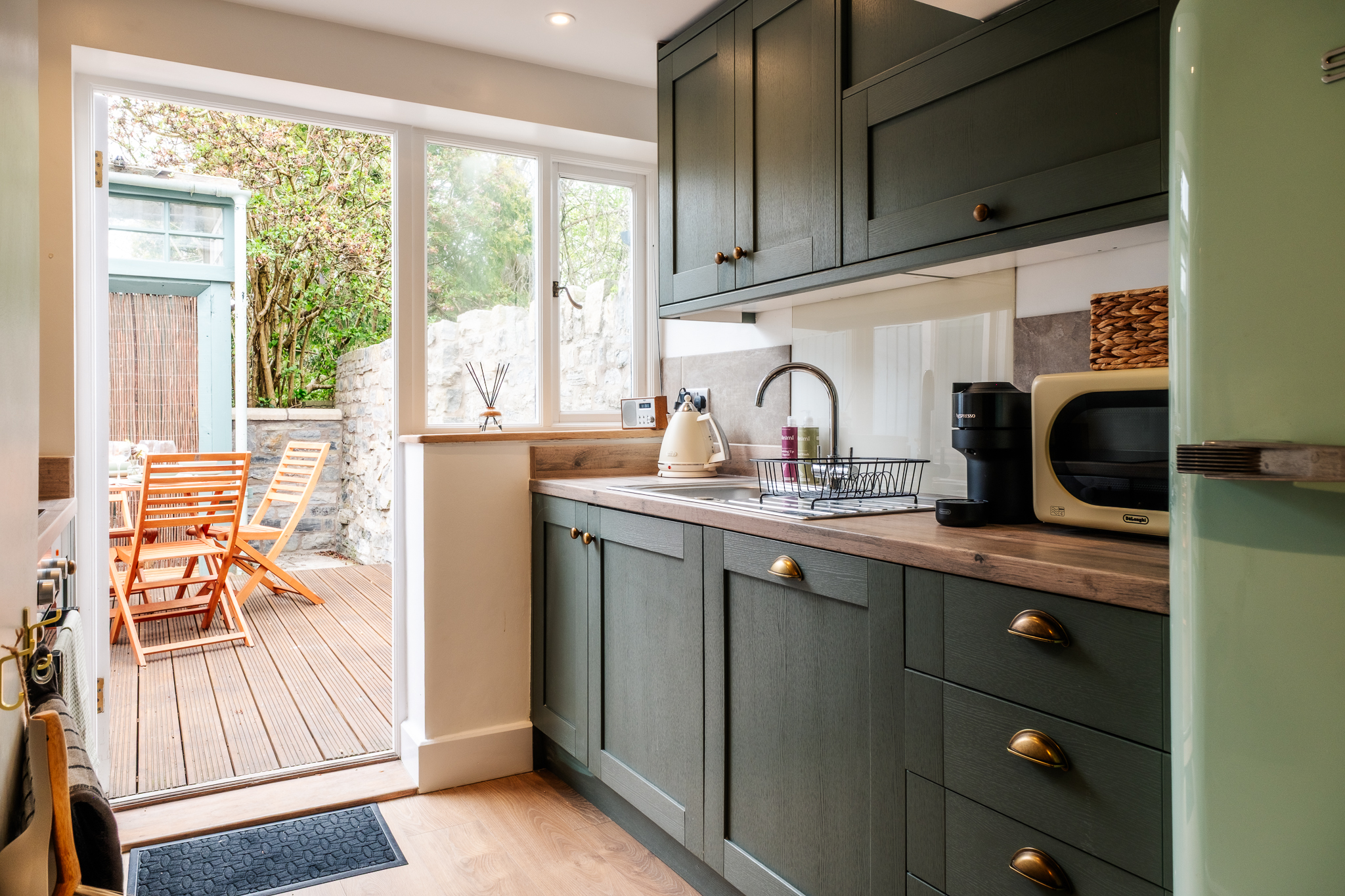 Sage green kitchen at No. 48 Magdalene Street with doors open onto the private deck