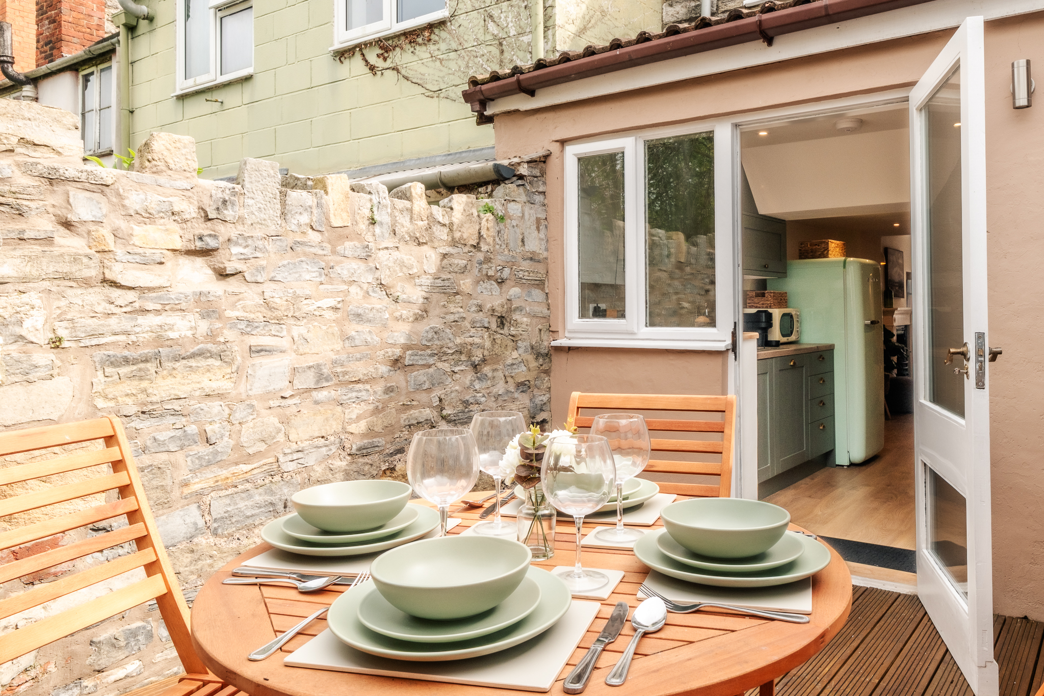Round wooden table on the private deck at No. 48 Magdalene Street laid with green tableware and wine glasses, the kitchen doors open behind it