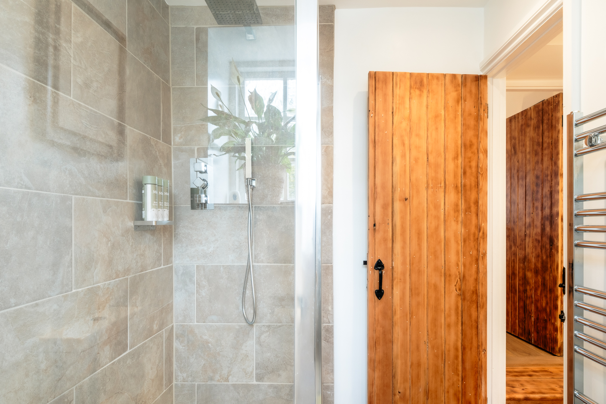Walk-in shower at No. 48 Magdalene Street with stone-effect tiles, a rainfall head and the original pine latch door alongside