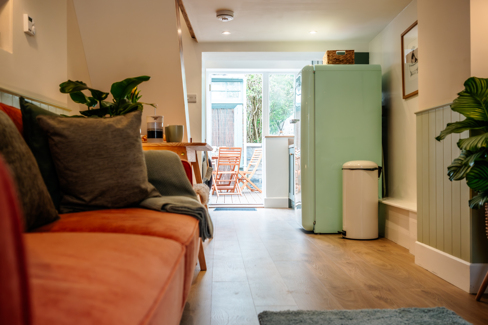 Open living space at No. 48 Magdalene Street with a terracotta sofa and a view through to the green kitchen and deck beyond
