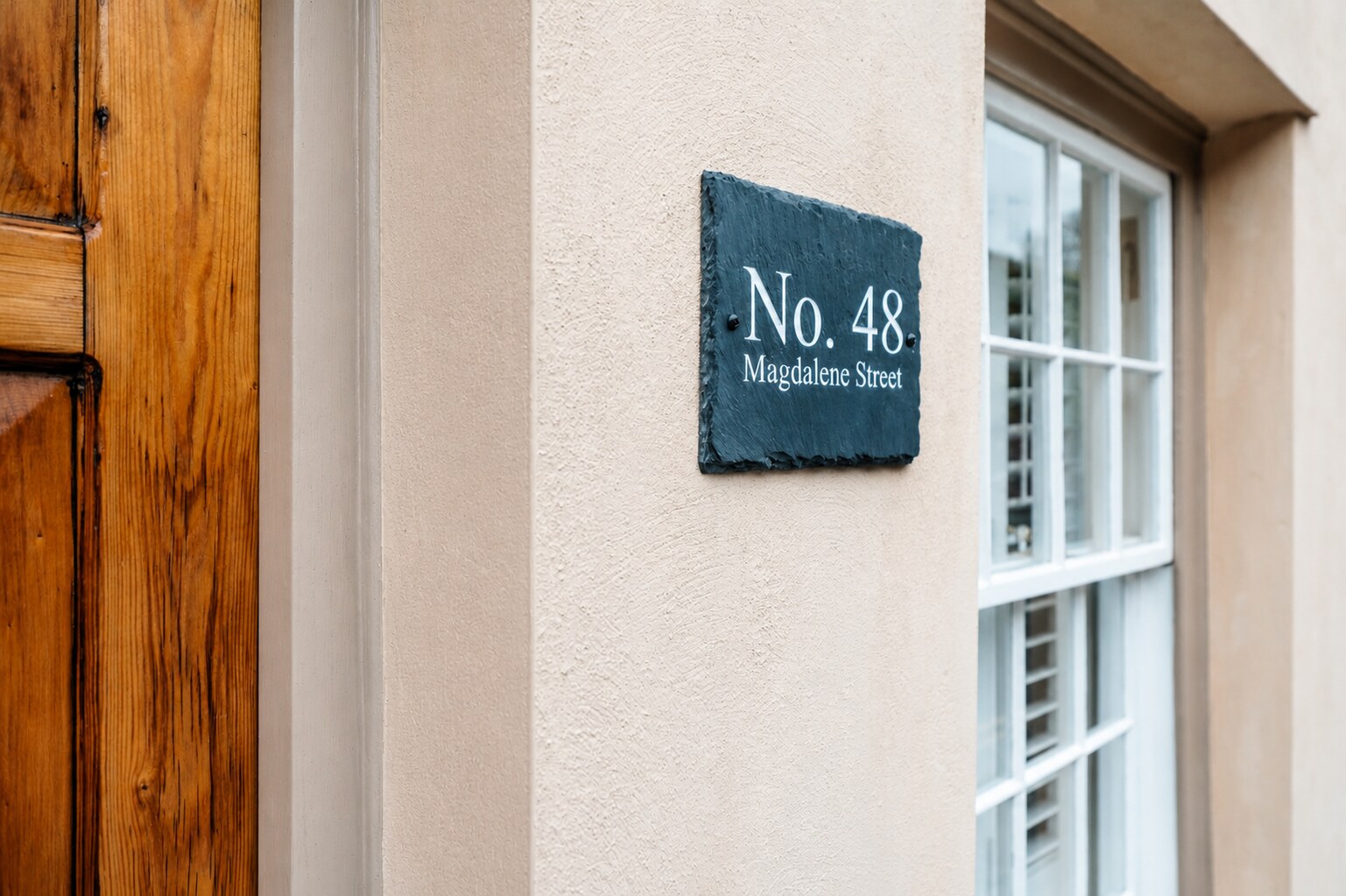 Slate house sign reading No. 48 Magdalene Street on the wall beside the cottage's front door